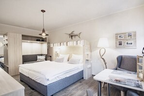 Una habitación de hotel con cama, escritorio, silla, lámpara y estante en la pared.