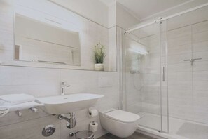 Un baño moderno con lavamanos, inodoro y ducha con mampara de vidrio.