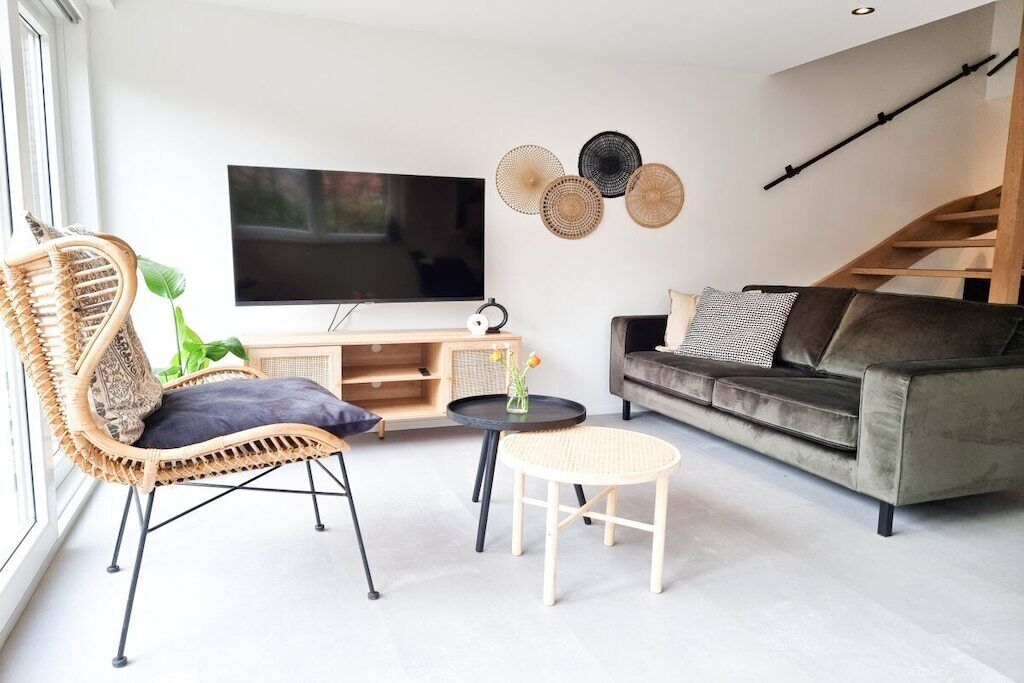 Ein modernes Wohnzimmer mit Fernseher, Korbmöbeln, einer Couch und einer Treppe.
