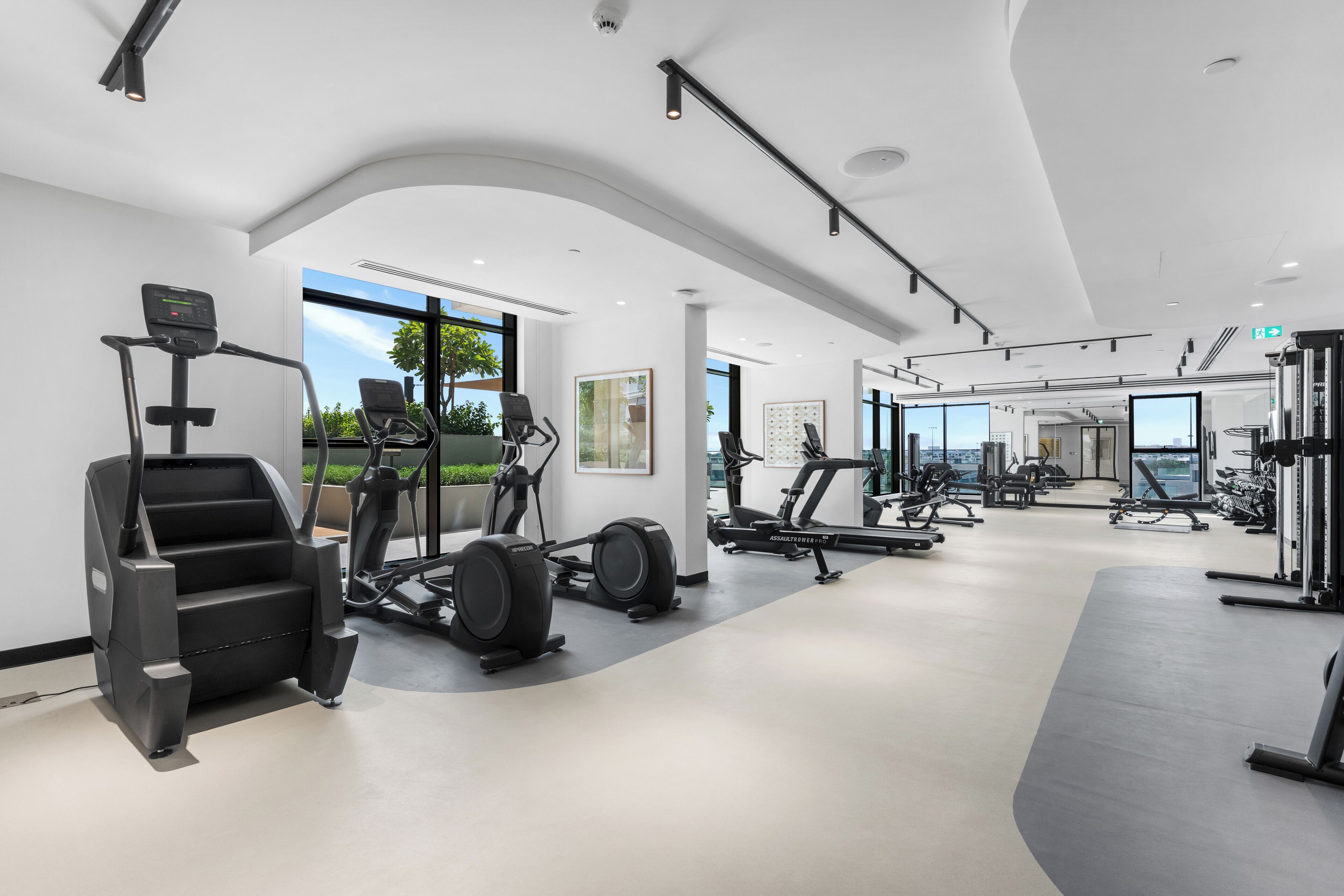 Un gimnasio moderno con diversos equipos de ejercicio, ventanas amplias y un diseño espacioso y limpio.