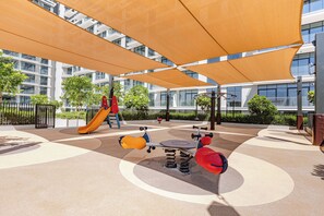 An outdoor play area with a slide, swings, and a climbing structure. - StayShort - Refined Classy 1 Bedroom in Dubai Hills - Sleeps 4! (Dubai Hills)