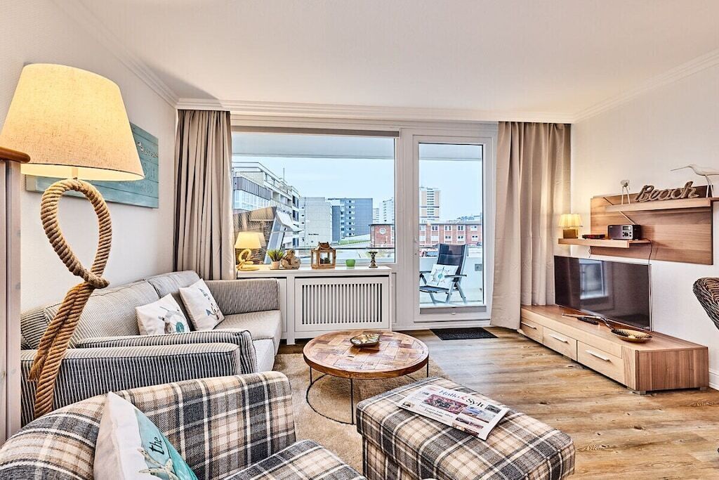 Una sala de estar moderna con sofá, reposapiés y mesa de centro, televisor y vistas de la ciudad a través de amplios ventanales.