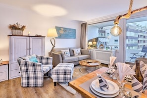 A modern living room with a sofa, two armchairs, a coffee table, and a dining area set for a meal. - Apartment in Westerland with swimming pool (Westerland)