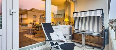 A balcony with a chair, a small table, and a striped awning.