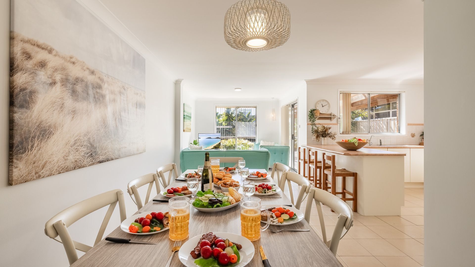 Un coin repas avec une table mise pour le repas, une cuisine en arrière-plan et une vue sur l’extérieur par une fenêtre.