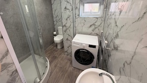 Un baño con cabina de ducha de vidrio, inodoro, lavadora y lavamanos.