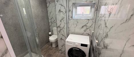 A bathroom with a glass shower enclosure, a toilet, a washing machine, and a sink.