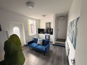 A compact living space with a kitchenette, a sofa, and a door leading to a bathroom.