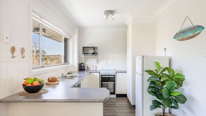 A modern kitchen with a large window, a microwave, a stove, and a refrigerator. - Sunset Shores 1 Surf Air , 24 Marine Dr - air con , Wi-Fi, across to the beach (Fingal Bay)