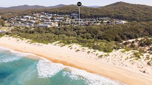 A coastal residential area with a beach, houses, and a sign indicating 'McGrath Nelson Bay Accommodation.' - Sunset Shores 1 Surf Air , 24 Marine Dr - air con , Wi-Fi, across to the beach (Fingal Bay)