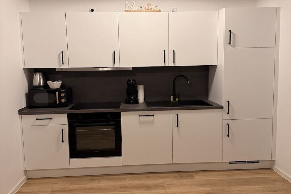 Een moderne keuken met witte kasten, een zwart aanrecht, een inbouwoven, een koffieapparaat en een spoelbak.