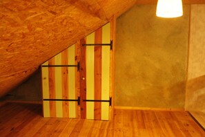 A room with wooden flooring, a sloped ceiling, and a door with vertical wooden planks.