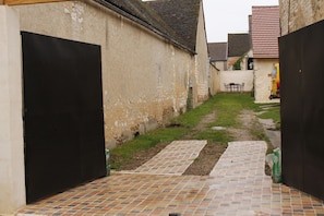 A narrow alleyway with a tiled path, a black gate, and a yellow vehicle in the background. - 3-bedroom vacation rental for 10 people with on-site Caribbean catering (Bellechaume)