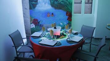 Een eettafel gedekt voor vier personen, met stoelen, een rode tafelkleed en een muurschildering van een waterval en tropisch landschap op de achtergrond.