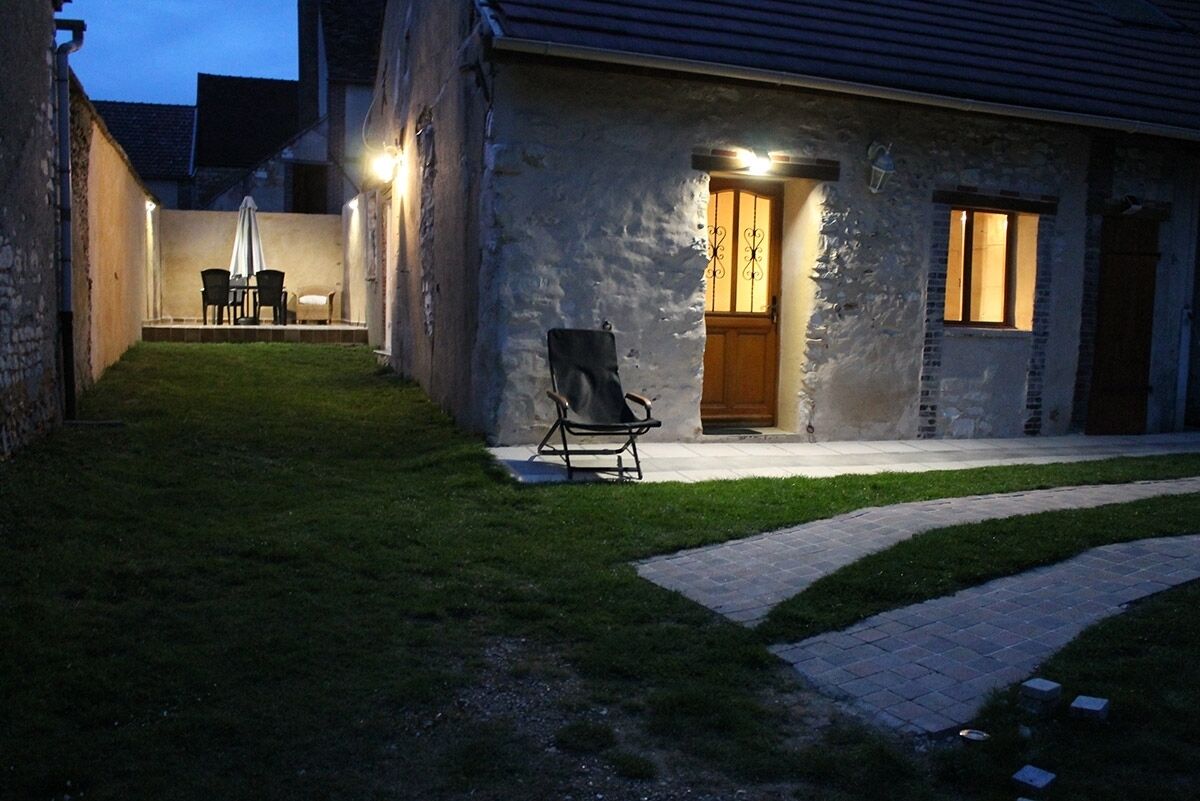 Un bâtiment en pierre doté d’une terrasse pavée, d’une chaise et d’une table avec des chaises.