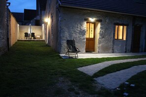 A stone building with a paved patio, a chair, and a table with chairs.