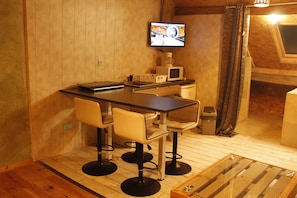 Una cucina compatta con un tavolo di legno, due sgabelli da bar, un forno a microonde e un televisore appeso al muro.