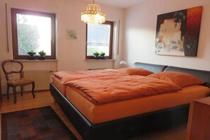 A bedroom with a bed, two windows with plants, a chair, a radiator, and a painting on the wall. - Holiday apartment in Konz with swimming pool (Konz)