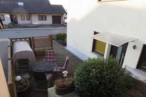 A patio with a table and chairs, a small garden, and a building in the background. - Holiday apartment in Konz with swimming pool (Konz)