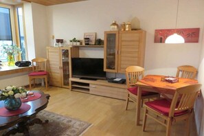 Un saló amb televisió, armaris de fusta, una taula de dinar amb cadires i una llar de foc.