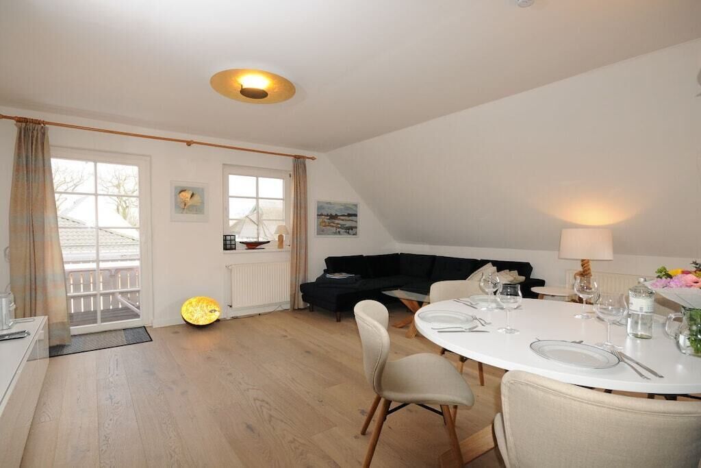 A dining area with a round table set for two, a black sofa, and a window with curtains.