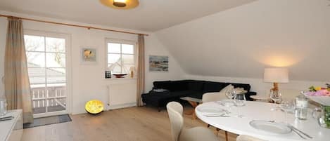 A dining area with a round table set for two, a black sofa, and a window with curtains.