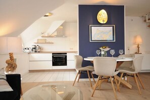 A modern kitchen with white cabinets, a black oven, and a dining area with a glass table and chairs. - Morning sun in Bültenhus (Born\/Darß)