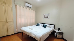 Ein Schlafzimmer mit Bett, Nachttisch, Wand-Klimaanlage und einem Fenster mit Vorhängen.