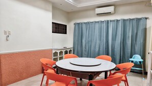 Ein Zimmer mit einem runden Tisch, sechs orangefarbenen Stühlen, einem blauen Vorhang und einem Hochstuhl für Babys.