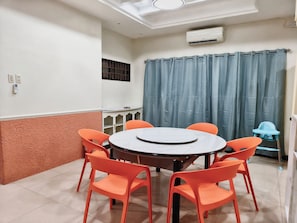 Et værelse med et rundt bord, seks orange stole, et blåt gardin og en babystol.