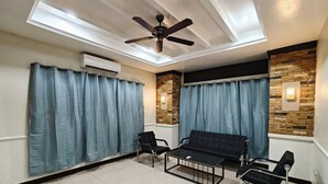 Ein modernes Wohnzimmer mit Deckenventilator, zwei schwarzen Sesseln, einer schwarzen Couch und einem Glastisch.