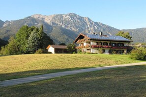 A house with a sloped roof and solar panels, surrounded by a grassy field and mountains. - Holiday apartment with 1 bedroom (Bad Reichenhall)