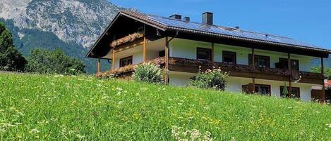 A two-story chalet with a sloped roof, solar panels, and a balcony with flower boxes.
