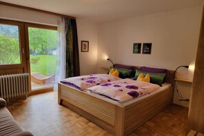 Un dormitorio con cama de madera, un radiador, una ventana con cortinas y vistas al exterior.