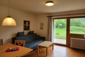 Una habitación con un sofá, una mesa, una lámpara colgante y una ventana con vistas a espacios verdes.