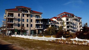 Un edifici residencial de diversos pisos amb balcons, una tanca blanca de palets i un cel serè.