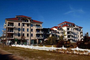 Un edificio residenziale a più piani con balconi, una recinzione bianca a stecche e cielo sereno.