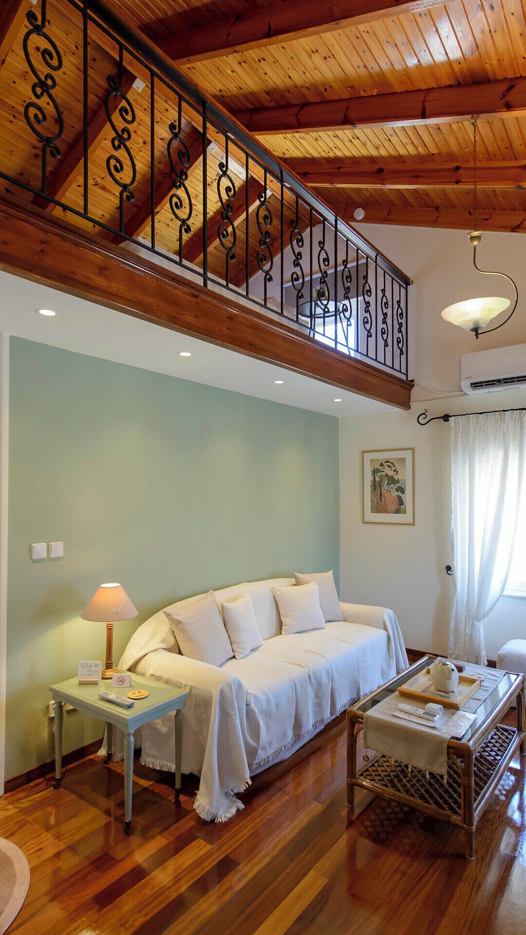 Une pièce avec un plafond en bois, un canapé blanc, une petite table avec une lampe et une rambarde décorative.