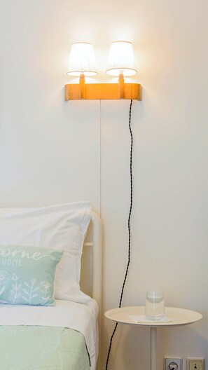 Een bed met een kussen, een nachtkastje met een glas water, en een wandlamp.