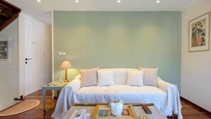 Een slaapkamer met een bed, nachtkastje, lamp en een schilderij aan de muur.
