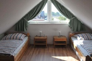 Une petite chambre mansardée avec deux lits simples, des tables de chevet en bois et une fenêtre avec des rideaux.