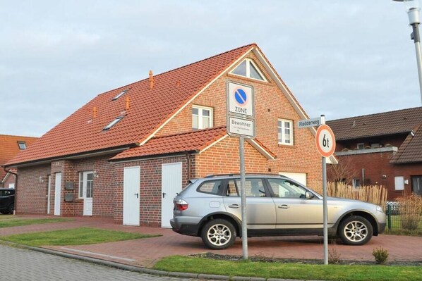 Un immeuble d’habitation avec un toit recouvert de tuiles rouges, une voiture garée et un panneau indiquant qu’il est interdit de se garer.