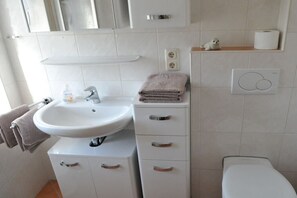 Une salle de bain avec un lavabo blanc, un miroir et des toilettes. On y trouve des serviettes et un distributeur de savon sur le lavabo.
