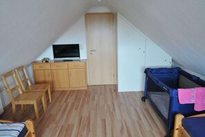 Une petite pièce mansardée triangulaire, avec un bureau en bois, une télévision, un lit superposé et une porte.