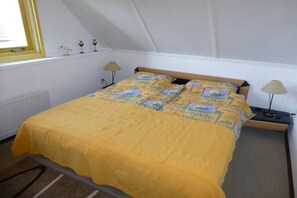 Una cama individual con una colcha amarilla, dos lámparas de noche y una ventana con marco amarillo.