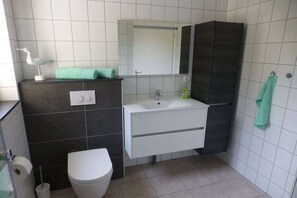Un baño con inodoro, lavamanos, espejo y toallero.