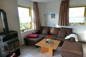 A living room with a fireplace, a sofa set, a coffee table, and a window with curtains. - Holiday home with 3 bedrooms (PD Julianadorp)