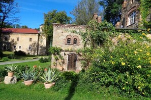 A historic stone building with a red roof, surrounded by lush greenery and flowering plants. - Manor house at the moated castle (Vierkirchen)