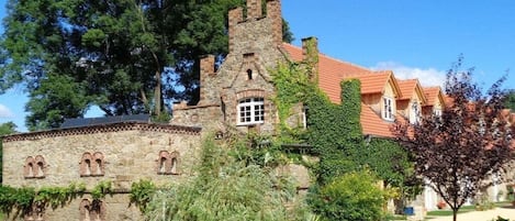 A historic stone building with a tower, surrounded by greenery and a clear sky.