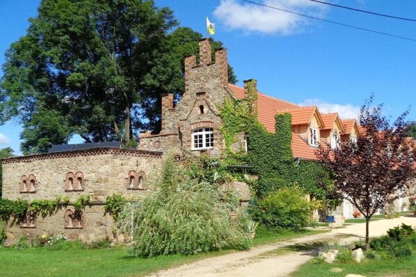 A historic stone building with a tower, surrounded by greenery and a clear sky. - Manor house at the moated castle (Vierkirchen)